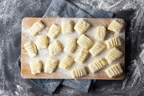 Raw uncooked homemade potato gnocchi with flour on cutting board. Top view. Dark background.