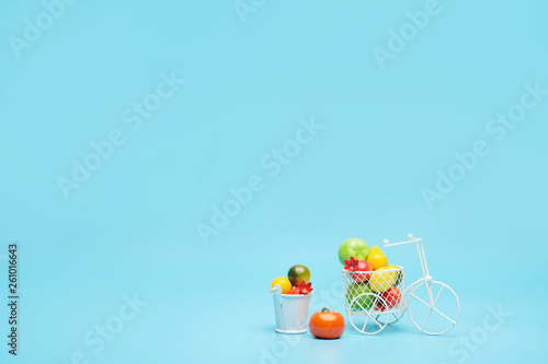 White wire bicycle with a basket filled with mini fruit. Near the bucket with vegetables and fruits. Blue background. Concept of harvesting and delivering fruits and vegetables.