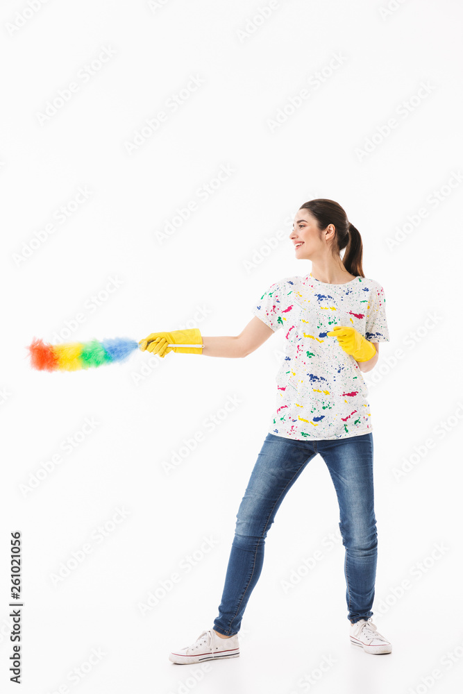 Photo of positive woman 20s wearing yellow rubber gloves holding colorful duster while cleaning room Photo of positive woman 20s wearing yellow rubber gloves holding colorful duster while cleaning room