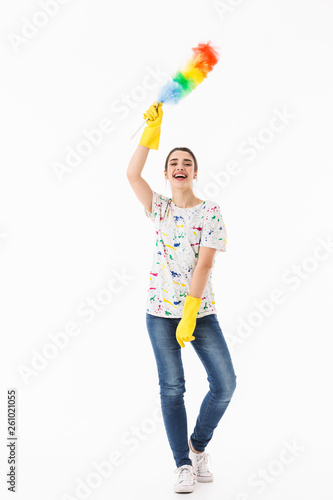 Photo of optimistic woman 20s wearing yellow rubber gloves holding colorful duster while cleaning room