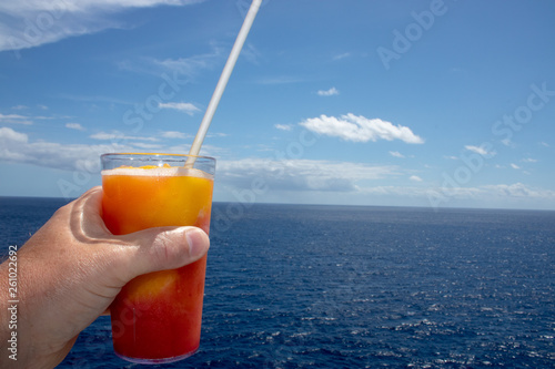 Close up of an orange & mango tropical cocktail overlooking a beautiful blue sky and sea.