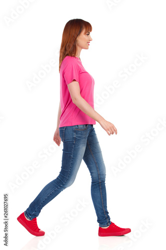 Side View Of Walking Young Woman In Pink Shirt, Jeans And Red Sneakers