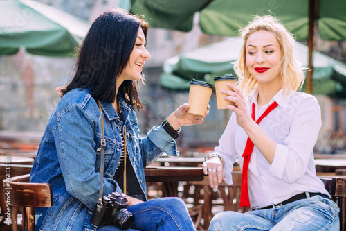 Two young stylish women with retro camera drinking coffee outside at street cafe. Outdoor lifestyle portrait concept. Copy space