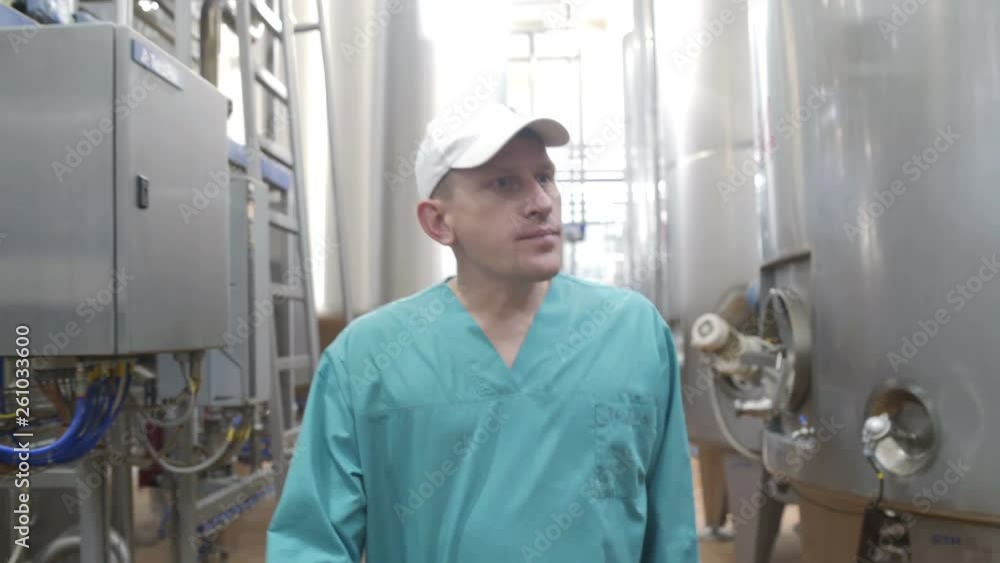 Food factory worker walks between equipment and monitors production at modern diary factory. Milk processing line Food factory worker walks between equipment and monitors production at modern diary factory. Milk processing line