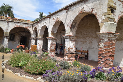 San Juan Capistrano, CA., U.S.A. Ap. 21, 2018. Mission courtyard, fired red brick pillared portico, fountains & water lilies, packed dirt, flat red brick-set paths, beautiful palms, trees & floral 