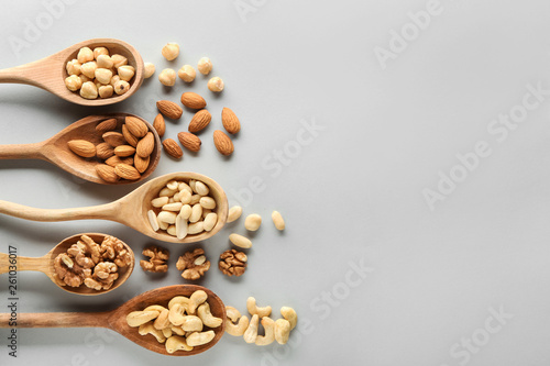 Spoons with different tasty nuts on light background