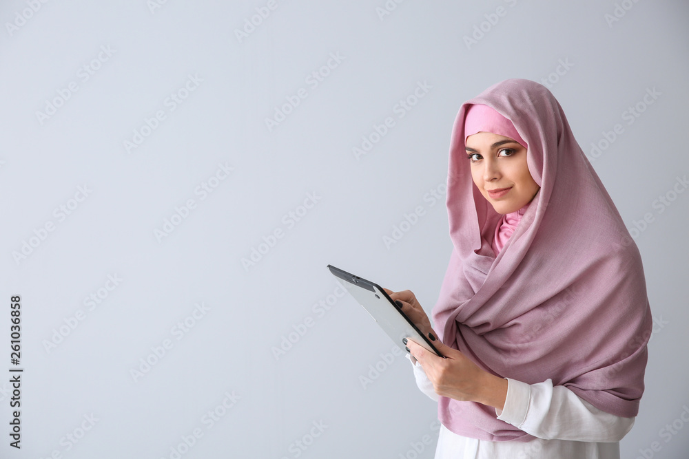 Young Muslim woman with tablet computer on light background Young Muslim woman with tablet computer on light background