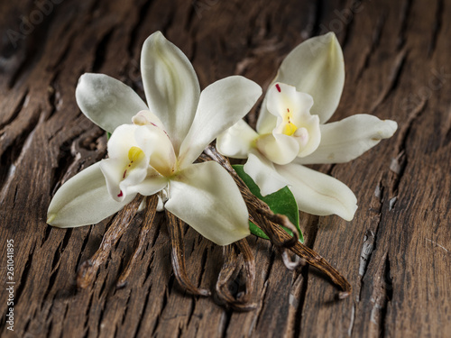 Dried vanilla sticks and vanilla orchid on wooden table.