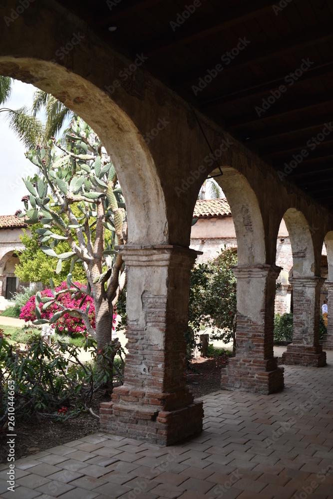 San Juan Capistrano, CA., U.S.A. Ap. 21, 2018. Mission courtyard, fired red brick pillared portico, fountains & water lilies, packed dirt, flat red brick-set paths, beautiful palms, trees & floral 