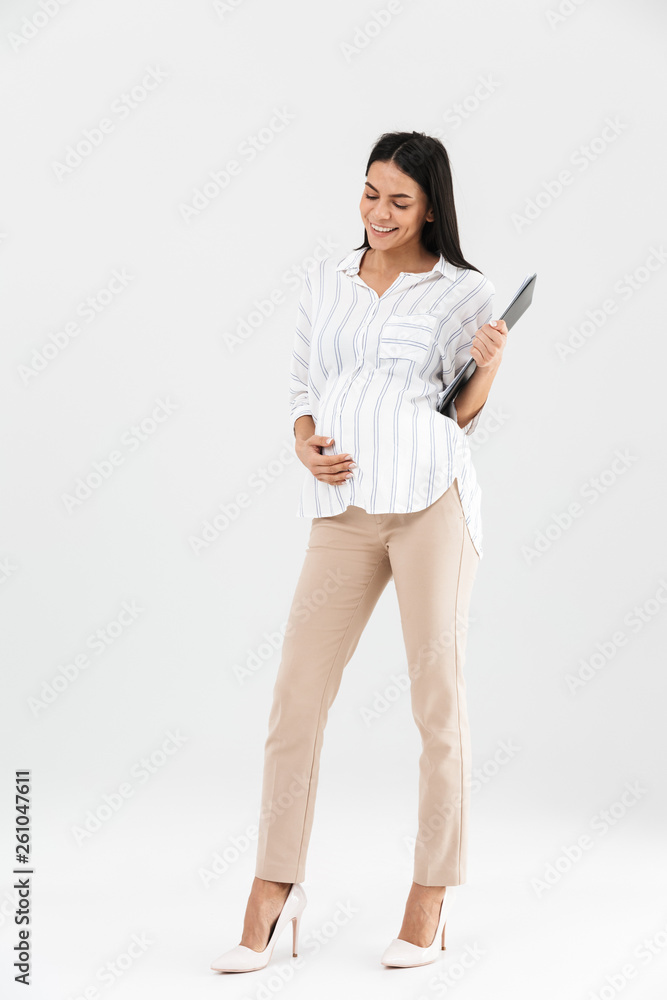 Full length photo of european pregnant businesswoman 30s holding clipboard and touching her big tummy Full length photo of european pregnant businesswoman 30s holding clipboard and touching her big tummy