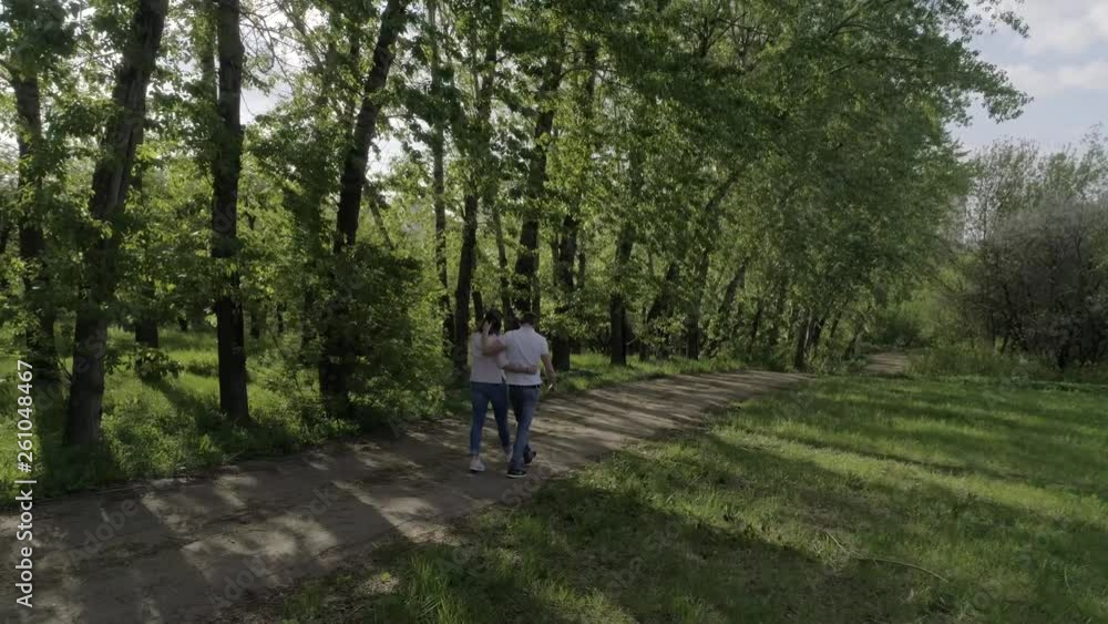 Lovers (man and woman) dressed in blue jeans and white t-shirts , holding hands, hugging, walking on a sandy road, shooting from the back, summer/spring Sunny day Lovers (man and woman) dressed in blue jeans and white t-shirts , holding hands, hugging, walking on a sandy road, shooting from the back, summer/spring Sunny day