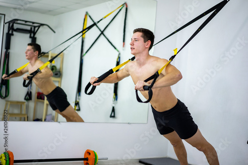 Beautiful young sports man are working out with TRX in gym