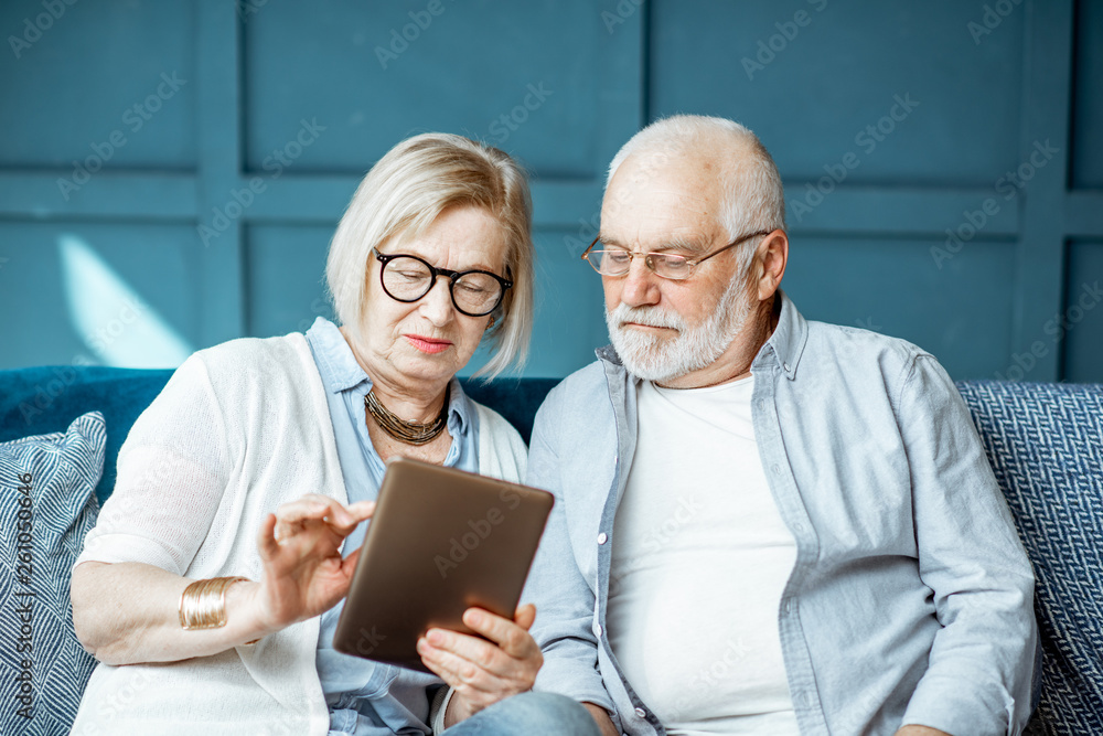 Lovely senior couple dressed casually using digital tablet while sitting together on the comfortable couch at home Lovely senior couple dressed casually using digital tablet while sitting together on the comfortable couch at home
