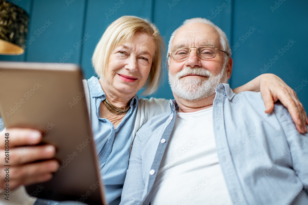 Portrait of a lovely senior couple sitting together with digital tablet on the comfortable couch at home Portrait of a lovely senior couple sitting together with digital tablet on the comfortable couch at home
