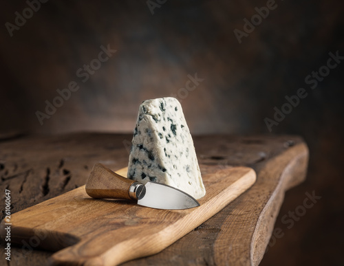 Piece of blue cheese and cheese knife on the wooden board. Dark background.