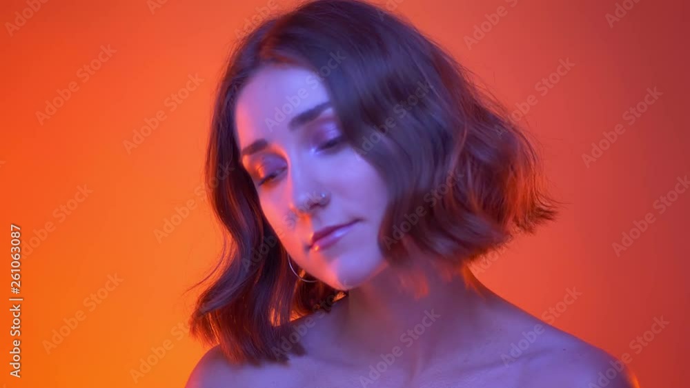 Closeup side view shoot of young attractive caucasian female with nose piercing turning to camera with neon red background Closeup side view shoot of young attractive caucasian female with nose piercing turning to camera with neon red background