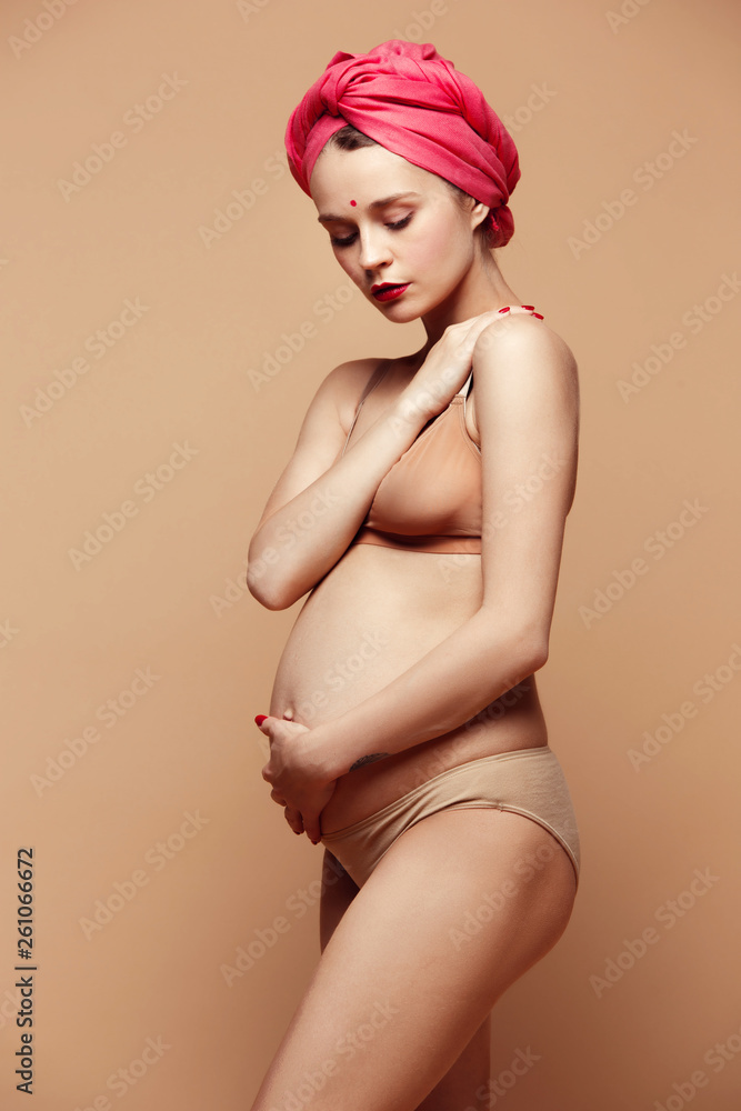 Young beautiful pregnant woman posing on brown background. Happy caucasian female model standing at studio. Pregnancy, parent, maternity, mothers day, parenthood and family concept. Young beautiful pregnant woman posing on brown background. Happy caucasian female model standing at studio. Pregnancy, parent, maternity, mothers day, parenthood and family concept.