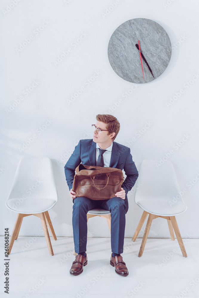 Fototapeta premium worried man in glasses holding briefcase while waiting job interview
