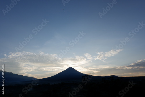 the view of the sun rises from behind the mountain, with a blue cloud background