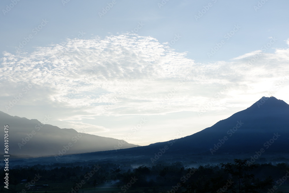 the view of the sun rises from behind the mountain, with a blue cloud background