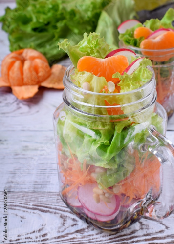 Layered salad in a jar with mandarins, radish, lettuce leaves, carrot and dressing