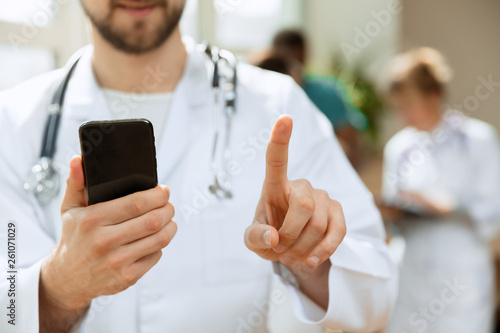 Professional caucasian male doctor with phone at hospital office or clinic. Medical technology and doctor staff service concept. Male finger touching empty search bar - can be used for insert text or