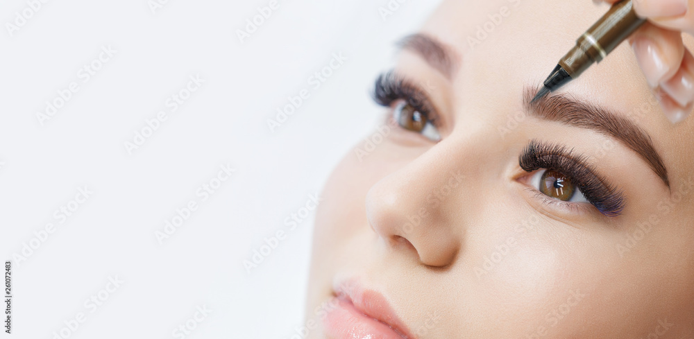 Beautiful young girl with long eyelashes tweezing her eyebrows in a beauty salon. Woman doing eyebrow permanent makeup correction . Microblading brow.