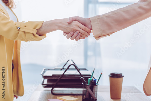 cropped view of employee and recruiter shaking hands in office near paper cup
