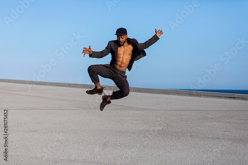 Front view young black man wearing casual clothes jumping in urban background.