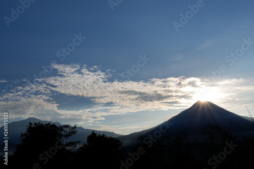 the view of the sun rises from behind the mountain, with a blue cloud background © andi