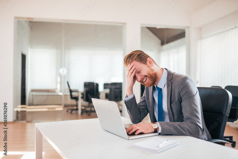 Ginger businessman laughing while using laptop at the office. Ginger businessman laughing while using laptop at the office.