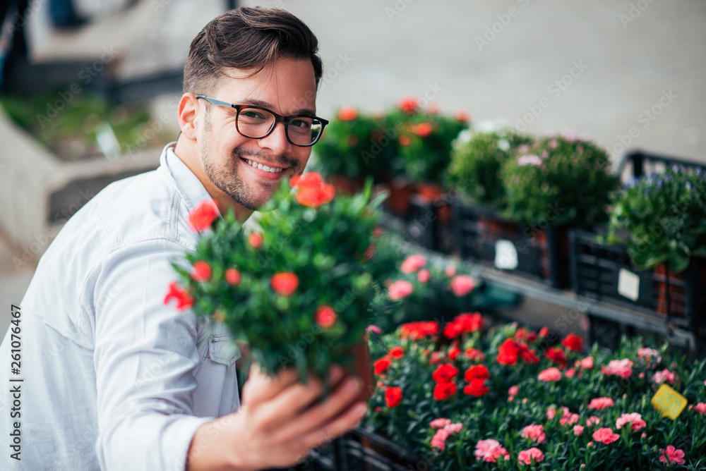 Happy young man holding flowers toward camera and smiling outdoors.