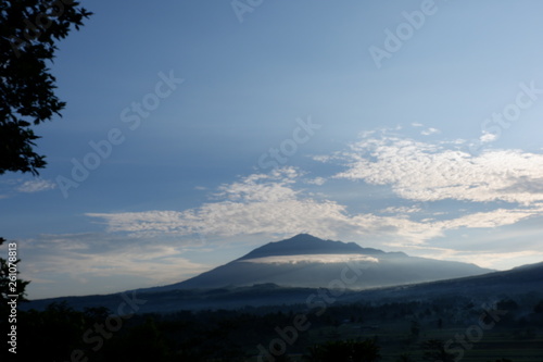 the view of the sun rises from behind the mountain, with a blue cloud background