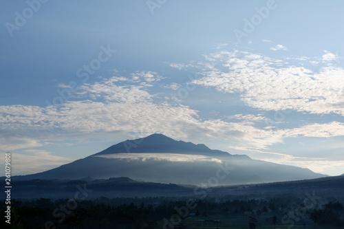the view of the sun rises from behind the mountain, with a blue cloud background