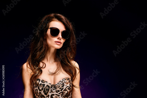 Confident young fit curvy woman in sunglasses and leopard bodysuit posing on studio background. Animal print