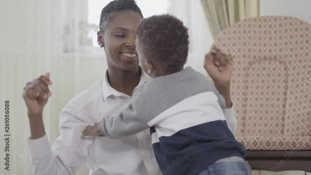 Joyful confident beautiful african american woman tickling her cute little son and laughing in cozy living room Joyful confident beautiful african american woman tickling her cute little son and laughing in cozy living room