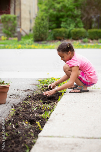 Portrait of a young child in pink, bending down and picking weeds from a garden. photo