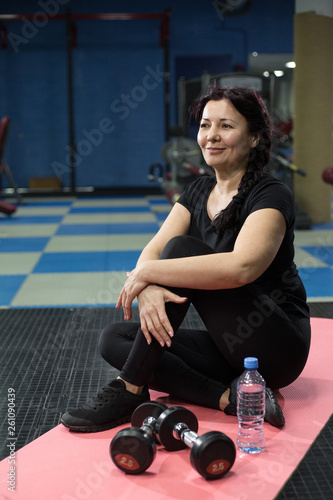 Fototapeta Naklejka Na Ścianę i Meble -  Senior woman in the gym sitting on a pink yoga mat. close-up. copy space.
