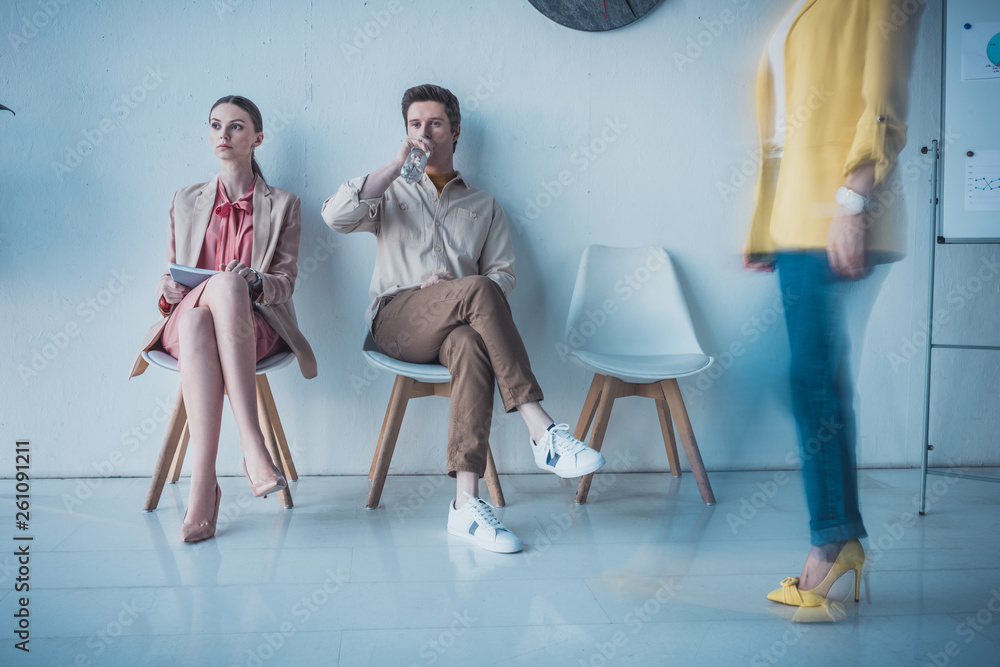 Fototapeta premium handsome employee drinking water while sitting with attractive woman