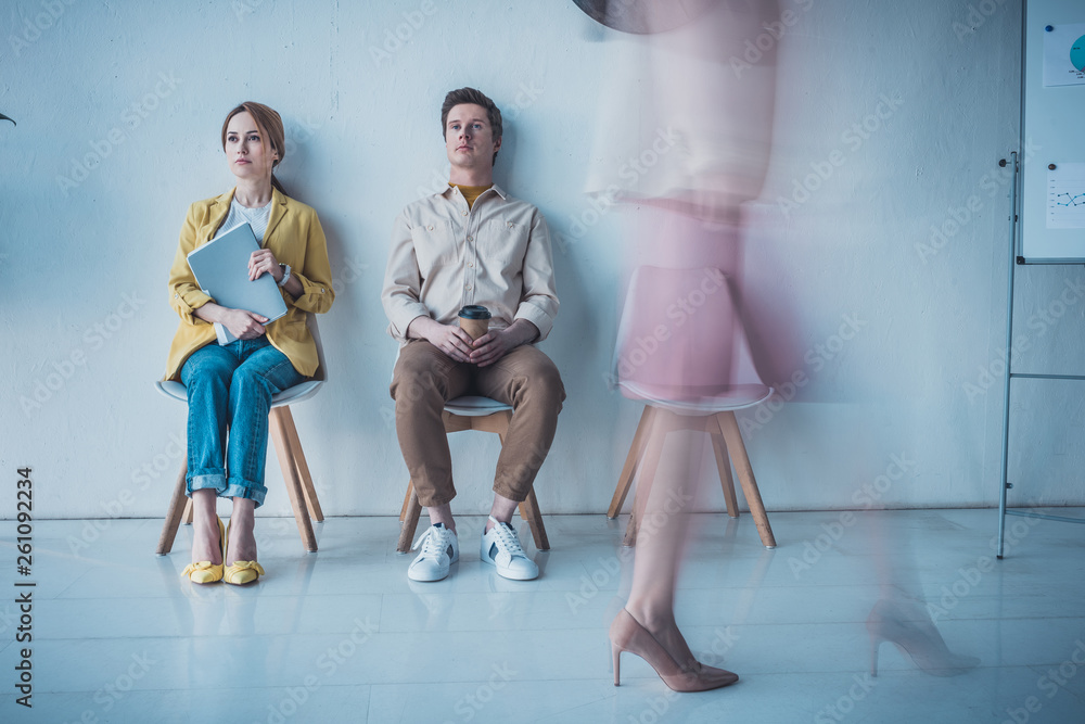 Fototapeta premium handsome man with paper cup sitting near attractive employee holding folder