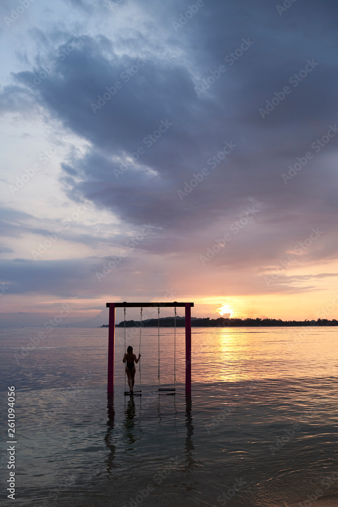 Traveler enjoying the sunset standing in a swing into water. On holidays. Traveler enjoying the sunset standing in a swing into water. On holidays.