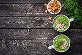 Broccoli cream soup. Vegetable green puree in two large white cup. Diet vegan soup of broccoli, zucchini, green peas on dark wooden background, banner, copy space, top view
