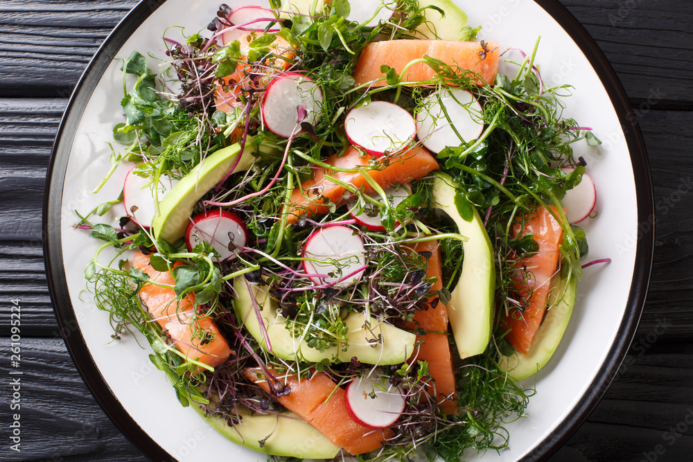 Freshly prepared salad of red fish, avocado, radish and a mix of micro green close-up on a plate. horizontal top view