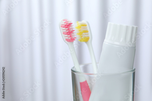 Glass with brushes and toothpaste on blurred background. Space for text
