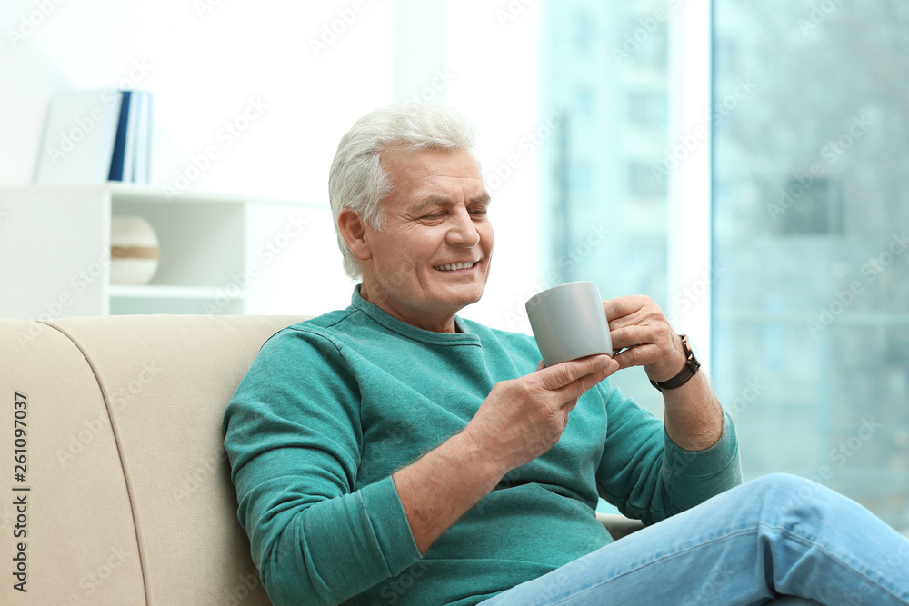 Portrait of mature man with cup of drink on sofa indoors Portrait of mature man with cup of drink on sofa indoors