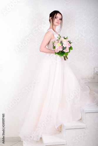 Slim beautiful woman wearing luxurious wedding dress over white studio background. Gorgeous bride holding flowers.