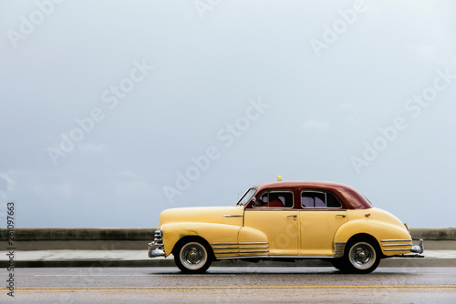 Yellow shiny retro car with white roof riding on street of tropi