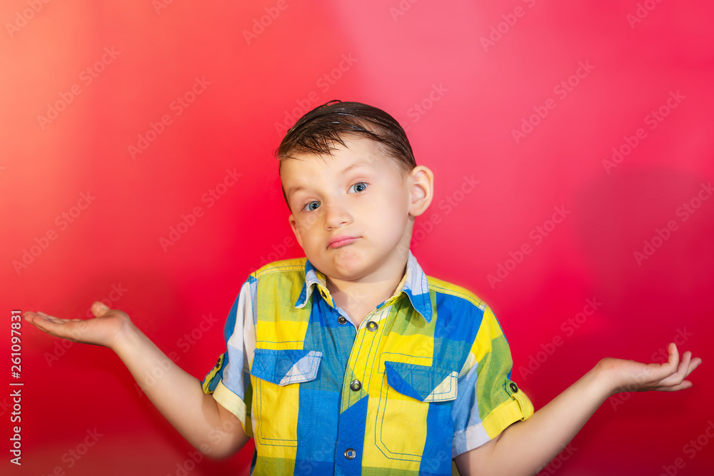 A boy in a color shirt shrugs and spreads his arms to the side, on a red background A boy in a color shirt shrugs and spreads his arms to the side, on a red background