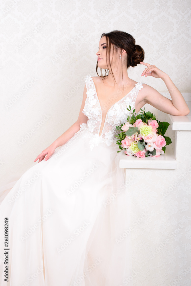 Slim beautiful woman wearing luxurious wedding dress over white studio background. Gorgeous bride holding flowers. Slim beautiful woman wearing luxurious wedding dress over white studio background. Gorgeous bride holding flowers.