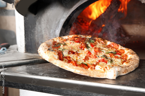 Taking out tasty pizza from oven in restaurant kitchen photo